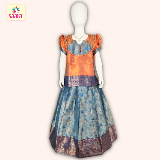 This Pattu Pavadai features a Orange blouse with Aari work, puffed sleeves and a matching Blue skirt made of floral stem designes jacquard fabric.